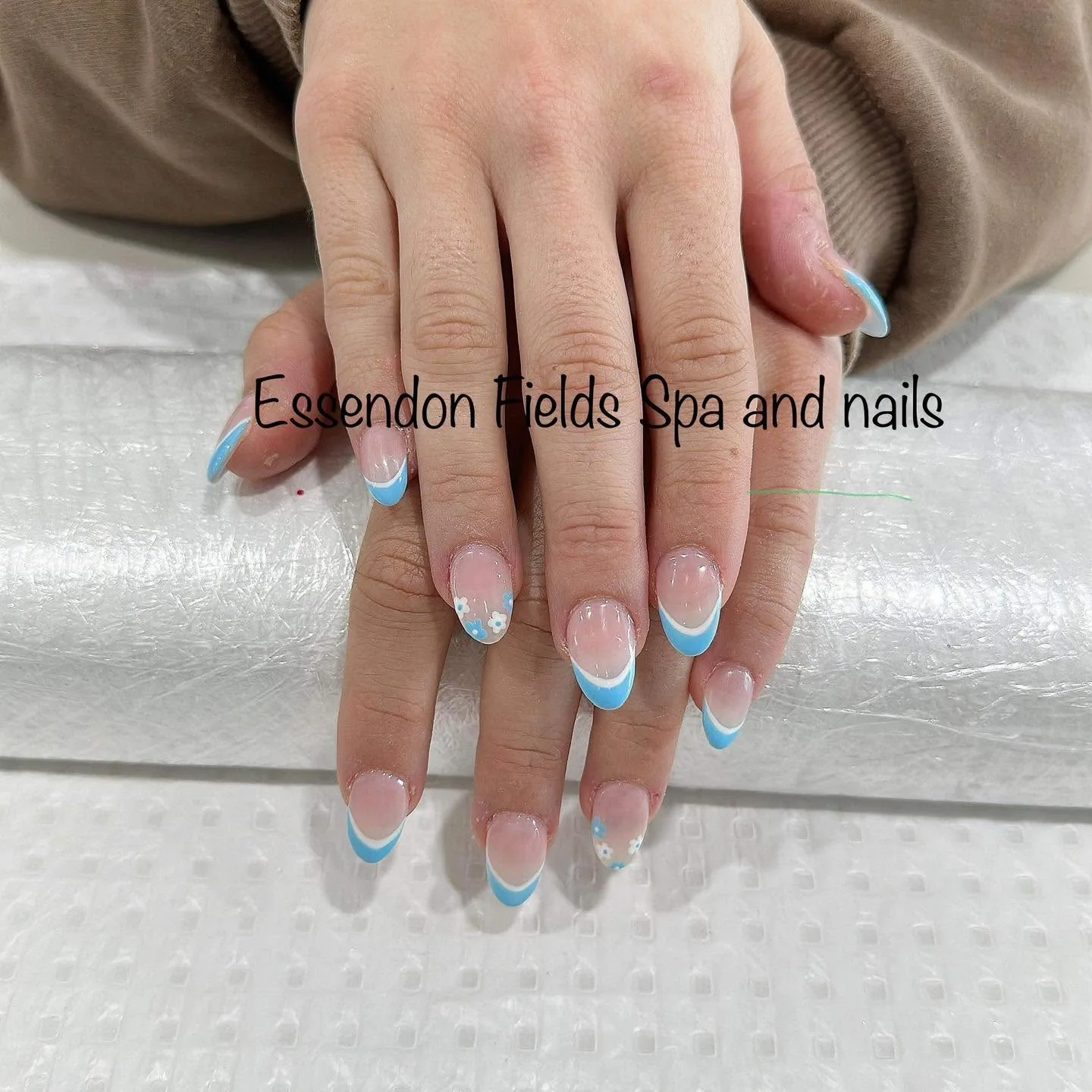 Almond nails in blue French tips with tiny white daisy accents, on tissue