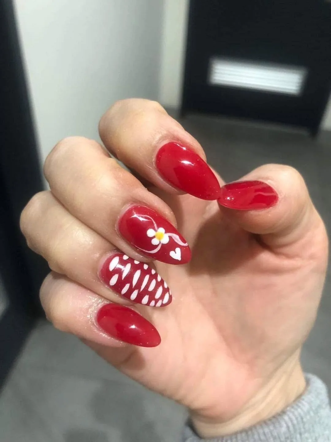 Red almond nails with white daisy and heart art and polka-dot accent nails, glossy, on grey studio backdrop