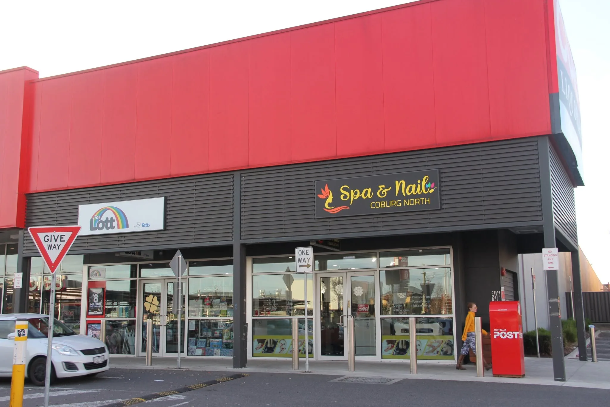The Spa & Nail Coburg North shopfront — illuminated flame-woman sign on the red-clad building inside Coburg North Village, with car park in front