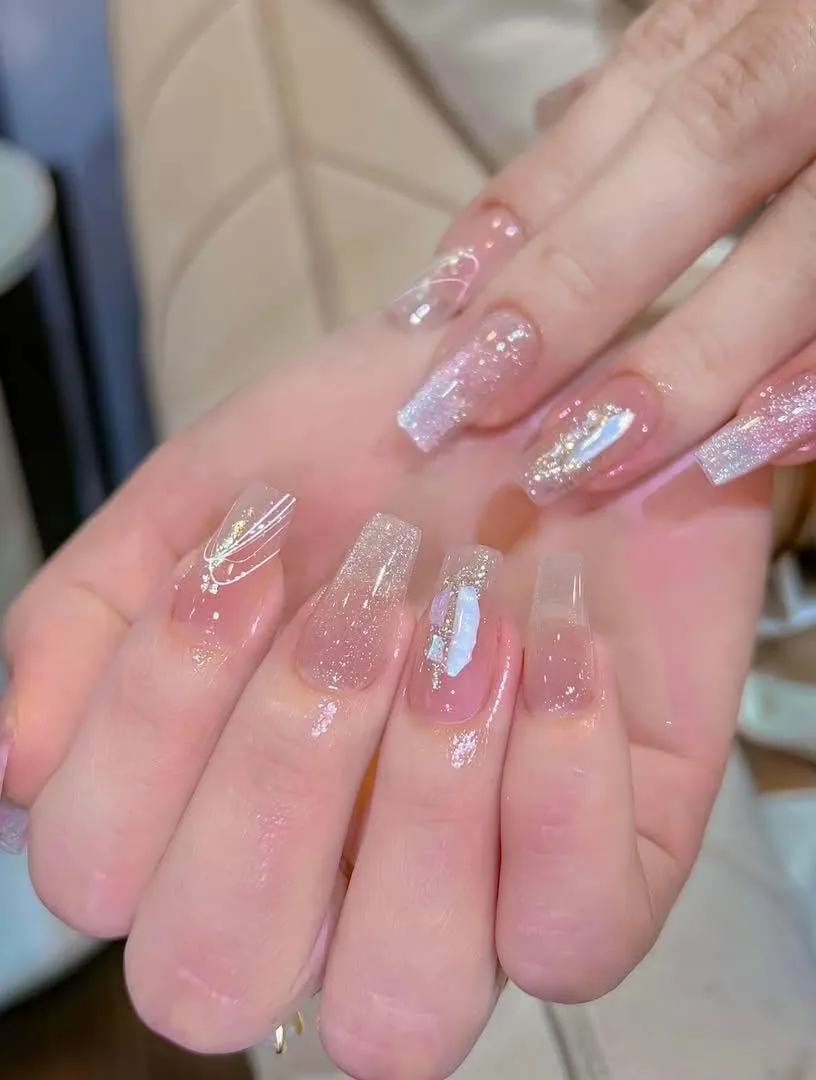 Coffin nails in sheer pink glazed jelly with glitter ombré and iridescent aura accents, on a cream chair