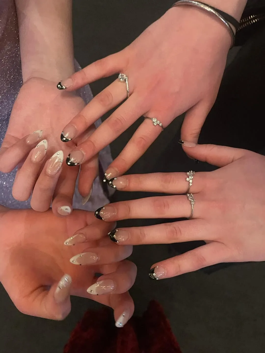 Several hands together with sheer-nude nails, black and chrome tips, rhinestones and silver rings