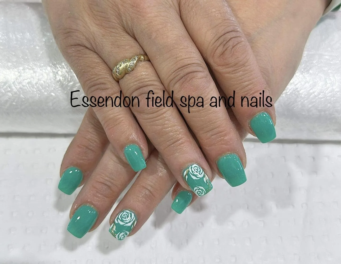 Square jade-green gel nails with two accents featuring white 3D rose art, gold twist ring, on white towel