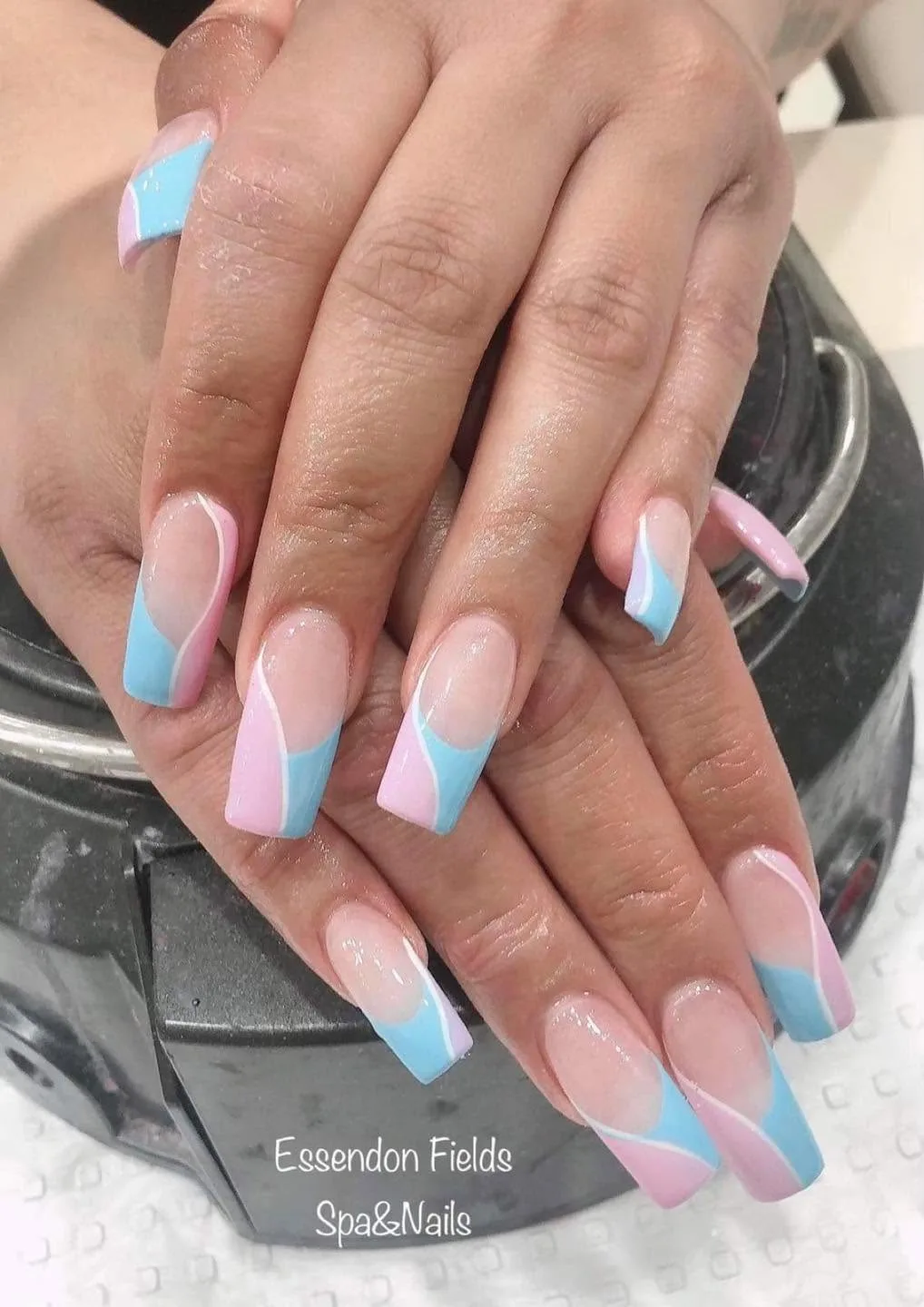 Long coffin nails in pink and blue candy-swirl French tips, on a black pedicure bowl