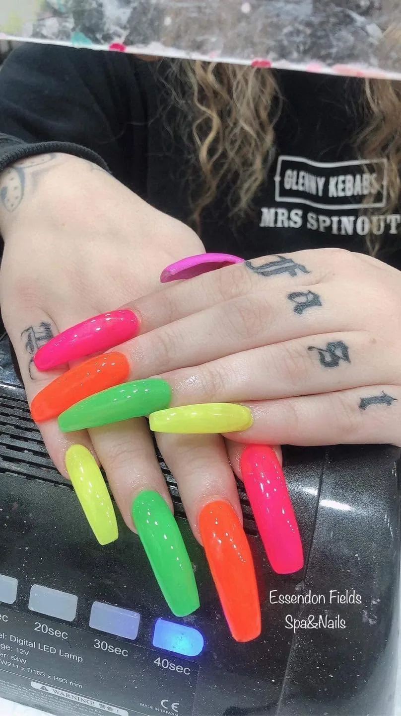 Long coffin neon-rainbow nails in pink, orange, green and yellow on a black LED lamp